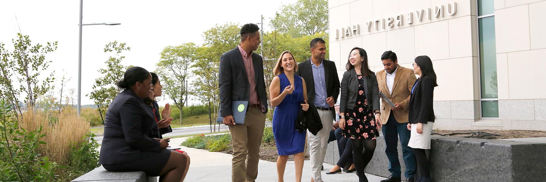 Business students walk and talk outside of University Hall.